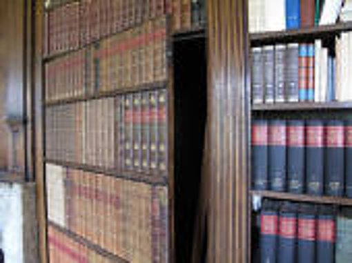 Une bibliothèque en bois remplie de livres anciens reliés, dont une section forme une porte secrète entrouverte sur une ouverture sombre.