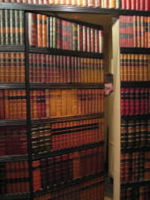 Une bibliothèque remplie de livres anciens à reliure de cuir dont une section entrouverte laisse apparaître une porte secrète.