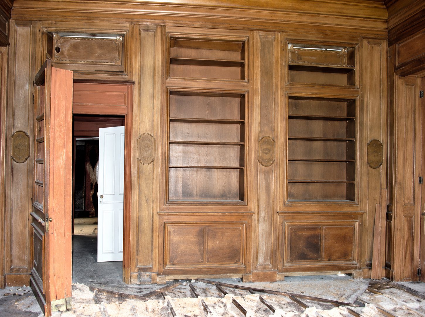 Une grande boiserie en bois clair avec des étagères encastrées et une porte orange ouverte, dans une pièce en cours de rénovation avec des bâches au sol.