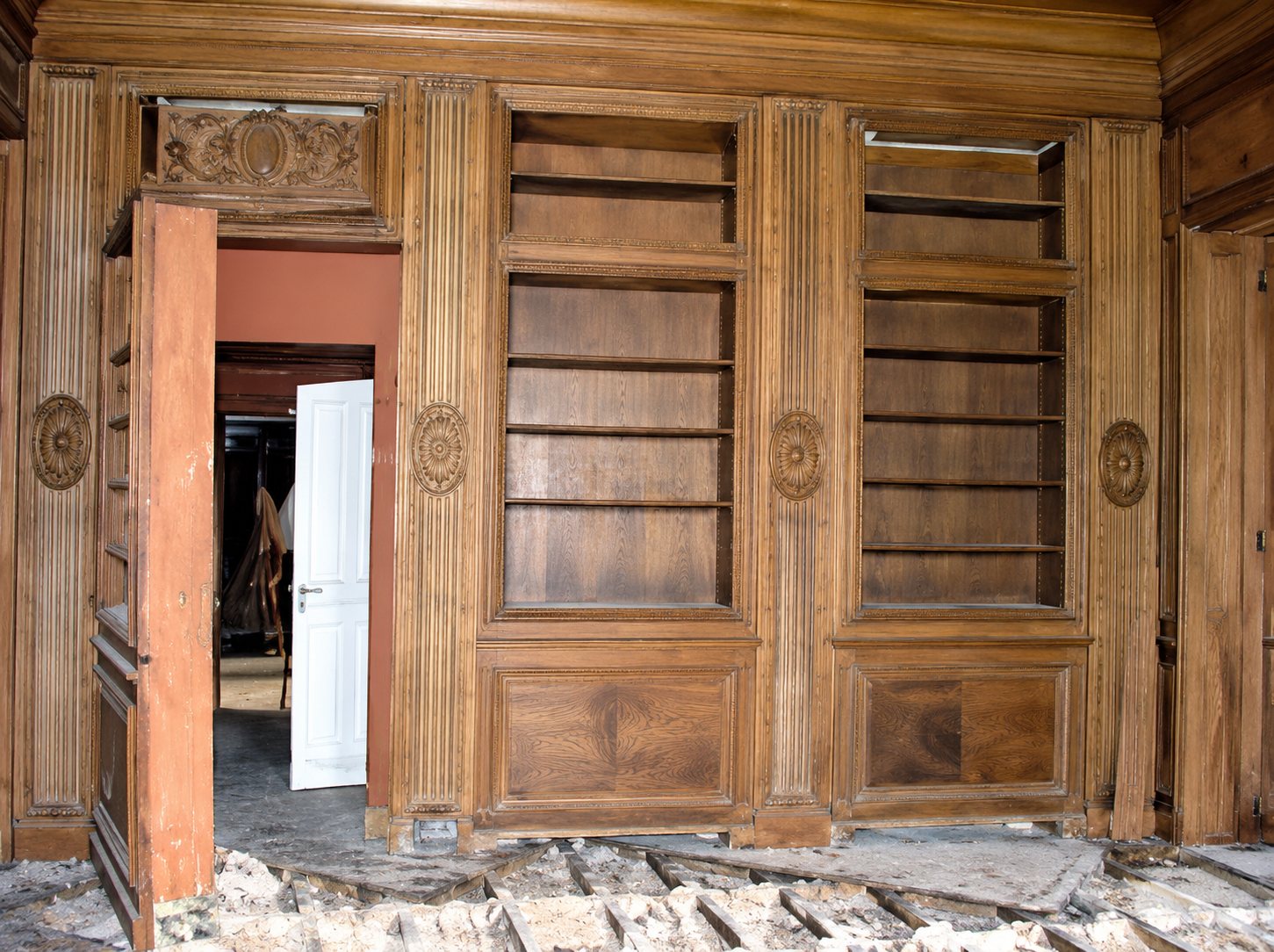 Une grande boiserie en bois avec des étagères intégrées et une porte orange ouverte, dans une pièce en cours de rénovation avec des bâches au sol.