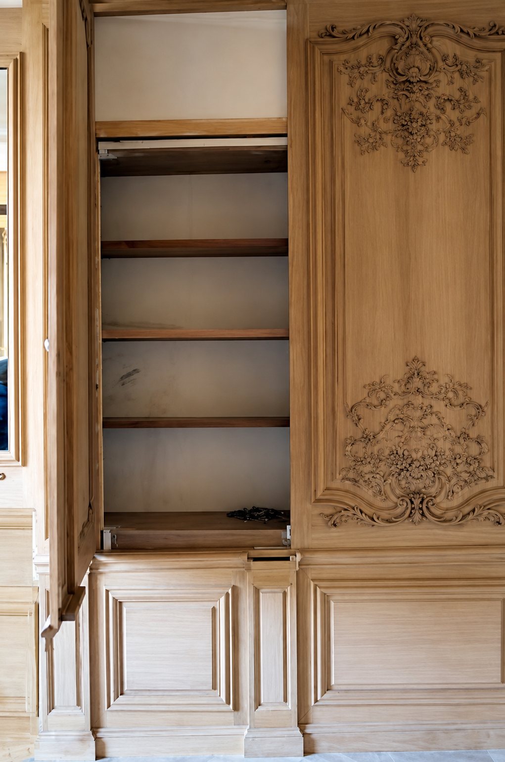 Boiserie en chêne non traité aux motifs sculptés, avec une porte ouverte sur un placard à étagères vides.