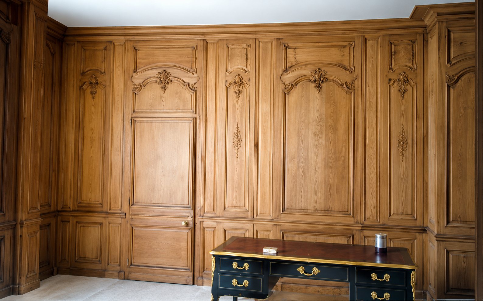 Une pièce entièrement habillée de boiseries en chêne clair sculptées, avec un bureau ancien posé devant le mur.