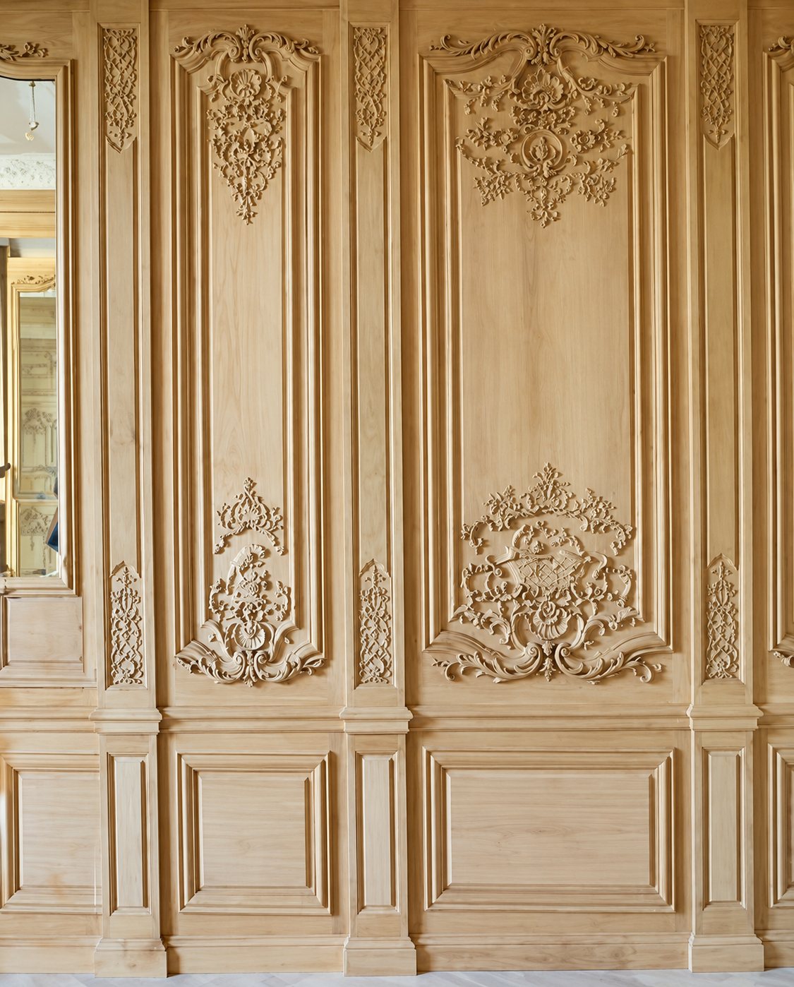Panneaux de boiseries en chêne clair non teinté, ornés de sculptures rocaille et de moulures, installés dans une pièce d'époque.